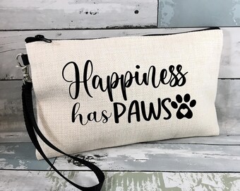 May include: Cream-colored canvas pouch with a black zipper and wrist strap. The text "Happiness has PAWS" is printed in black script and a paw print with a heart. The pouch is rectangular and has a black zipper.