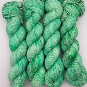 May include: Four skeins of green yarn with black speckles. The yarn is wound into a loose coil.