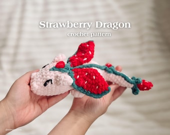 Puede incluir: Un dragón de fresa tejido a ganchillo con detalles rojos, blancos y verdes. El dragón tiene alas de fresa rojas y una columna vertebral verde. El texto "Strawberry Dragon crochet pattern" se muestra encima del dragón.
