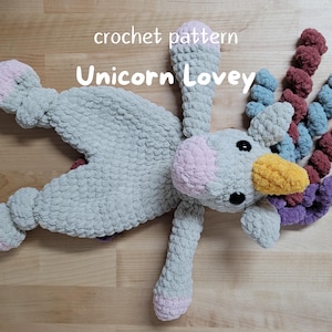 May include: A crocheted unicorn lovey with a gray body, pink hooves, and a yellow horn. The unicorn has a multi-colored yarn tail.