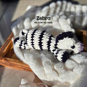 Może przedstawiać: Pluszowa zebra wykonana na szydełku w kolorze czarno-białym z wzorem bez szwów. Zebra leży na białym, puszystym kocu.
