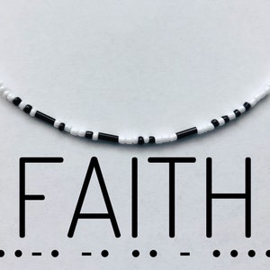 Könnte beinhalten: Schwarze und weiße Perlenkette mit dem Wort "FAITH" darunter. Die Kette liegt auf einem weißen Hintergrund.