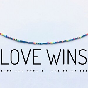 May include: A colorful beaded necklace with the words "LOVE WINS" printed below. The necklace is made of small, colorful beads strung on a black thread.