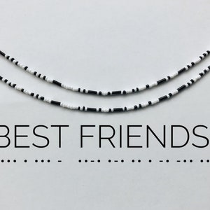 Könnte beinhalten: Zwei Freundschaftsarmbänder aus schwarzen und weißen Perlen. Die Armbänder liegen auf einer weißen Oberfläche. Unter den Armbändern steht der Text "BEST FRIENDS", gefolgt von einer Reihe von Punkten in Braille.