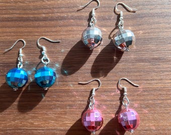 May include: Three pairs of disco ball earrings. One pair is silver, one pair is blue, and one pair is pink.