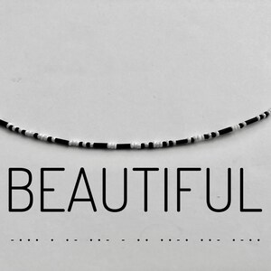 Könnte beinhalten: Eine schwarze und weiße Perlenkette mit dem Wort "BEAUTIFUL" darunter.