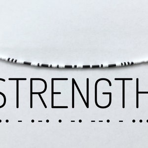 Könnte beinhalten: Eine schwarz-weiße Perlenkette mit dem Wort "STRENGTH" darunter gedruckt. Die Kette besteht aus kleinen, runden Perlen und hat ein schlichtes, minimalistisches Design.