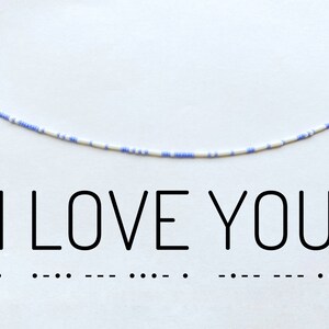 Könnte beinhalten: Eine weiße und hellblaue Perlenkette mit den Worten "I LOVE YOU" und Morsecode-Punkten und Strichen darunter.