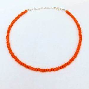 May include: A simple orange beaded choker necklace with a silver clasp.