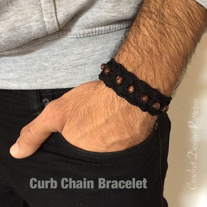 K&ouml;nnte beinhalten: Ein schwarzes H&auml;kelarmband mit einer Bord&uuml;renkette und braunen Holzperlen. Das Armband wird am Handgelenk getragen.