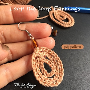May include: A pair of crocheted loop earrings in a peach color with a brown crystal bead on each earring. The earrings are held in a hand and the text "Loop the loop Earrings" is above the earrings. The text "pdf pattern" is in the lower right corner of the image.