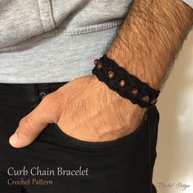 K&ouml;nnte beinhalten: Ein schwarzes H&auml;kelarmband mit einer Curb-Kette und braunen Holzperlen. Das Armband wird am Handgelenk getragen.