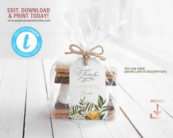 Può includere: Un'etichetta di ringraziamento stampabile con un design floreale e il testo "Grazie per aver coccolato il nostro piccolo con amore." L'etichetta è legata a un sacchetto di cellophane trasparente pieno di un dolce s'mores.