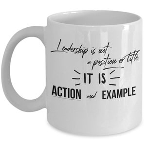 May include: White ceramic coffee mug with black text that reads "Leadership is not a position or title - IT IS - ACTION and EXAMPLE".