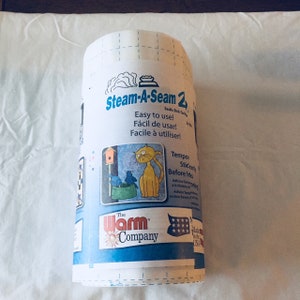 May include: A roll of Steam-A-Seam 2 double stick fusible web with a grid-lined paper backing. The label features the product name, The Warm Company logo, and a graphic of a yellow cat looking at two blue birds near a birdhouse on a post.
