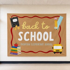 Peut inclure: Une toile de fond rectangulaire beige avec une bordure rouge ondulée et le texte back to SCHOOL FAIRVIEW ELEMENTARY SCHOOL. Les illustrations incluent un cahier noir, un crayon jaune, une règle bleue, une pile de livres avec une pomme et un bus scolaire jaune.
