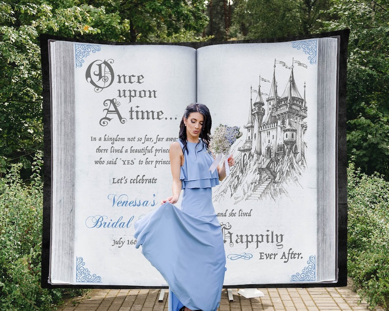 May include: A blue book with a white background and a drawing of a castle on the right page. The text on the left page reads "Once upon a time... In a kingdom not so far, far away there lived a beautiful prince who said "YES" to her prince Let's celebrate Venessa's Bridal July 16th and she lived Happily Ever After."