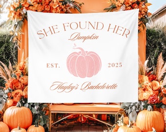 May include: White banner with the text "She Found Her Pumpkin Est. 2025 Hayley's Bachelorette" in orange lettering. The banner is decorated with a pink pumpkin illustration and is surrounded by orange and yellow flowers.