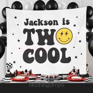 Op de afbeelding: Witte banner met zwarte tekst die "Jackson is TWO COOL" luidt met een gele smiley met bliksemschichten voor ogen. De banner is versierd met zwarte sterren.
