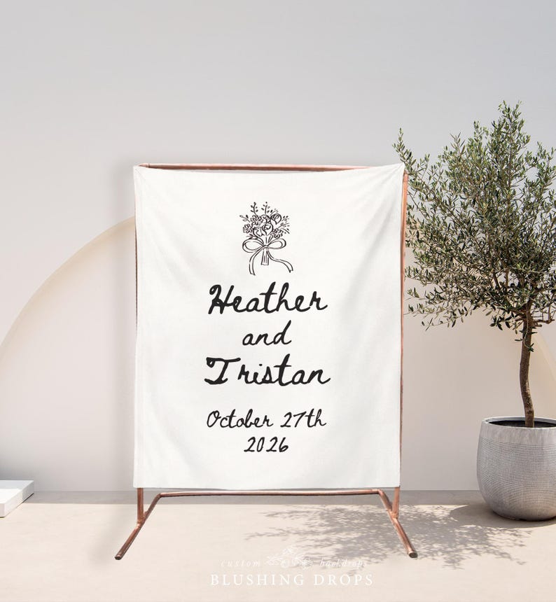 May include: A white fabric wedding sign with the names "Heather and Tristan" and the date "October 27th 2026" in black script. The sign is supported by a copper-colored metal frame, with a floral illustration at the top.
