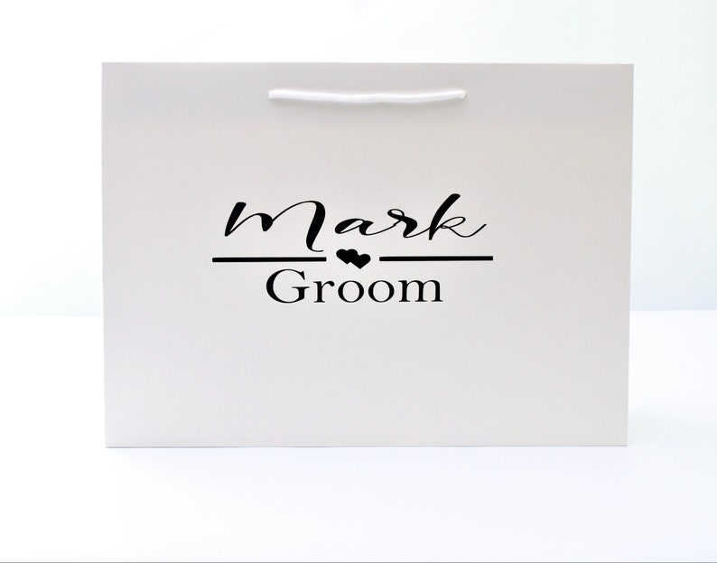 May include: White gift bag with black text that reads "Mark Groom" with two small hearts above the word "Groom".