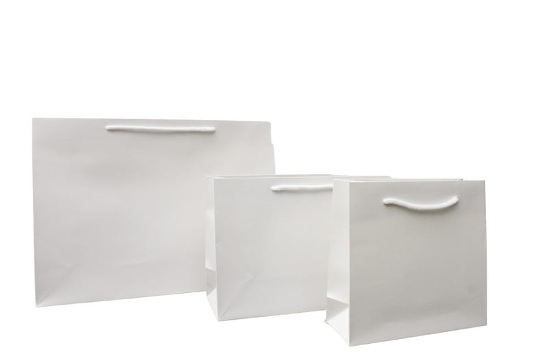 May include: Three white paper gift bags of different sizes with white rope handles.