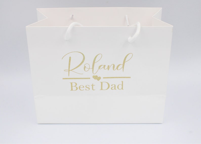 May include: White gift bag with gold lettering that says "Roland Best Dad" with two small hearts above the word "Best".