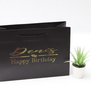 May include: Black gift bag with a gold inscription that reads "Denis Happy Birthday".