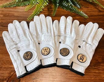 May include: Four white golf gloves with personalized wooden patches. The patches feature a crown with the letter "P", a wreath with the letters "JW", a wreath with the letters "JM", and the letter "T".