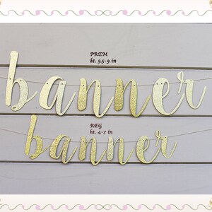 May include: Gold glitter banner with the word "banner" written in cursive. The banner is strung on a white string and is hanging on a light gray wooden wall. The text "PREM ht. 5.5-9 in" and "REG ht. 4-7 in" is written in black below the banner.