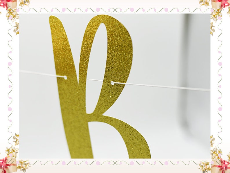 May include: Gold glitter letter "R" banner for a party or celebration. The letter is cut out of gold glitter paper and is strung on a white string.