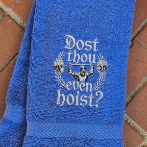 Puede incluir: Toalla de gimnasio azul con la frase bordada "Dost thou even hoist?" y un dise&ntilde;o de halterofilia. La toalla doblada tiene una apariencia texturizada, ideal para el gimnasio.