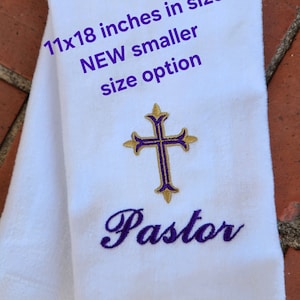 May include: White towel with an embroidered purple cross and the word "Pastor" in purple script. The towel measures 28x46 cm. Text on the towel reads "NEW smaller size option".