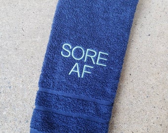 May include: A dark blue hand towel with the text "SORE AF" embroidered in light blue.