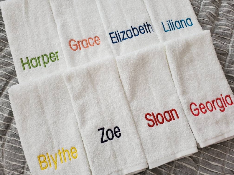 Może przedstawiać: Zestaw białych ręcznik&oacute;w z wyszytymi imionami w r&oacute;żnych kolorach, w tym Harper, Grace, Elizabeth, Liliana, Blythe, Zoe, Sloan i Georgia.