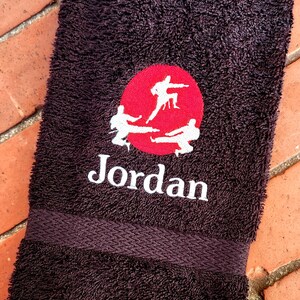 May include: A dark brown towel with a red circle and white embroidered figures. The text "Jordan" is embroidered in white below the circle.