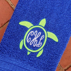 May include: A blue beach towel with a green embroidered turtle and the monogram "CJL" in white.