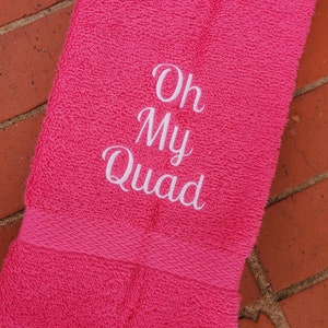 May include: Pink hand towel with white embroidery that says "Oh My Quad".