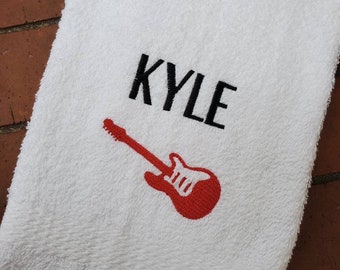 以下が含まれることがあります： 白いタオルに黒い刺繍で「KYLE」と、赤いギターのシルエットが刺繍されています。