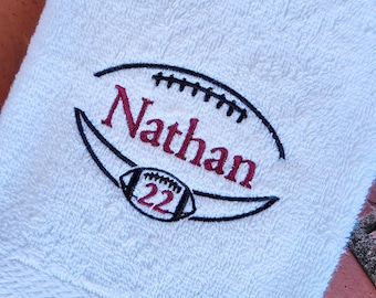 May include: White towel with a black and red embroidered football design. The football has the number 22 on it and the name "Nathan" is embroidered above it.