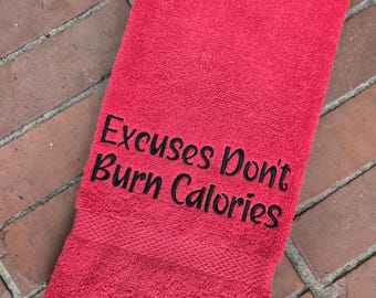 May include: A bright red towel with the embroidered text "Excuses Don't Burn Calories" in black. The towel is made of a soft, absorbent material, perfect for the gym or home use. The towel is rectangular and folded.
