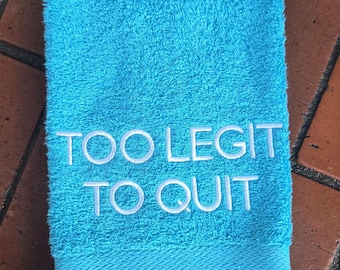 May include: A turquoise blue towel with white embroidered text that reads "Too Legit To Quit".