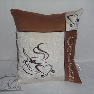 May include: A brown and beige throw pillow with embroidered coffee cup and the word "Coffee" on it.