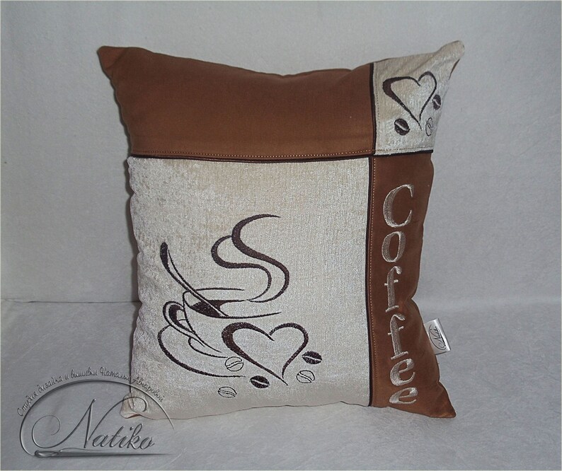 May include: A brown and beige throw pillow with embroidered coffee cup and the word "Coffee" on it.