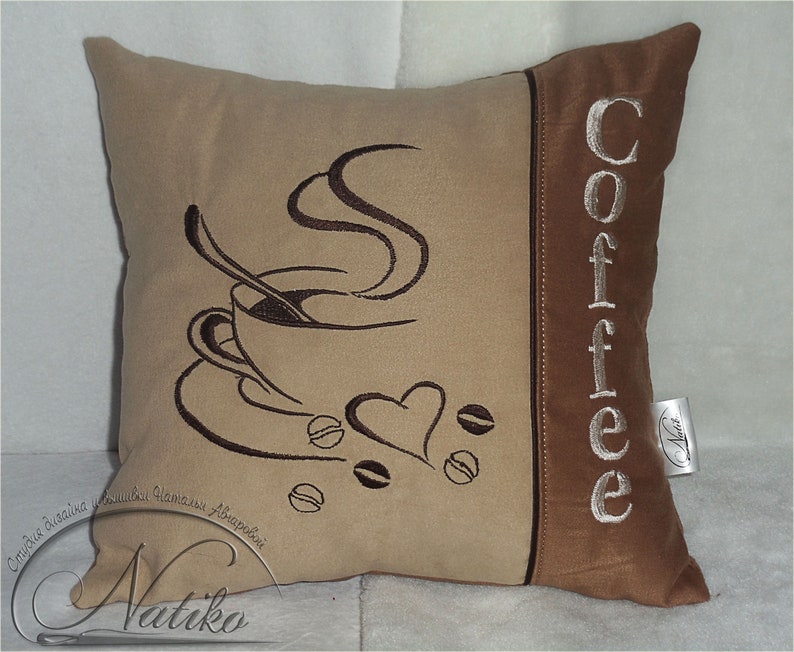 May include: A brown and beige throw pillow with embroidered coffee cup and steam design. The word "Coffee" is embroidered on the side of the pillow in white.
