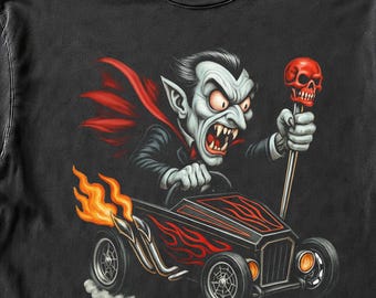 May include: A black short-sleeve t-shirt featuring a graphic of a cartoon vampire with a red cape driving a black hot rod with red flame details. The vampire holds a gear shift topped with a red skull. The design includes orange exhaust flames.