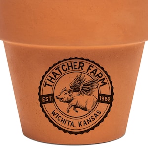 May include: A potted succulent plant with pale green leaves and red tips. The plant is in a terracotta pot with a black logo that reads "Thatcher Farm" and "Wichita, Kansas."
