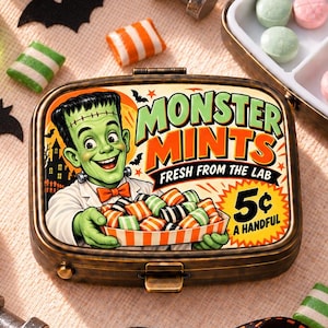 May include: A rectangular metal tin labeled Monster Mints Fresh From The Lab 5 cents a handful, featuring a Frankenstein illustration. The tin is surrounded by small orange pumpkins, green liquid in a beaker, black paper bats, and striped candies.