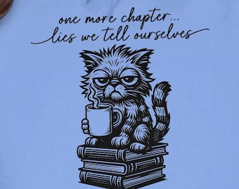 May include: A light blue hoodie featuring a black and white illustration of a grumpy cat holding a coffee mug, sitting on a stack of books. The text "one more chapter... lies we tell ourselves" is above the cat.