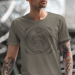 Puede incluir: Una camiseta gris con un gr&aacute;fico de un cangrejo dentro de un c&iacute;rculo con estrellas y otras formas geom&eacute;tricas. El gr&aacute;fico est&aacute; en blanco y negro.